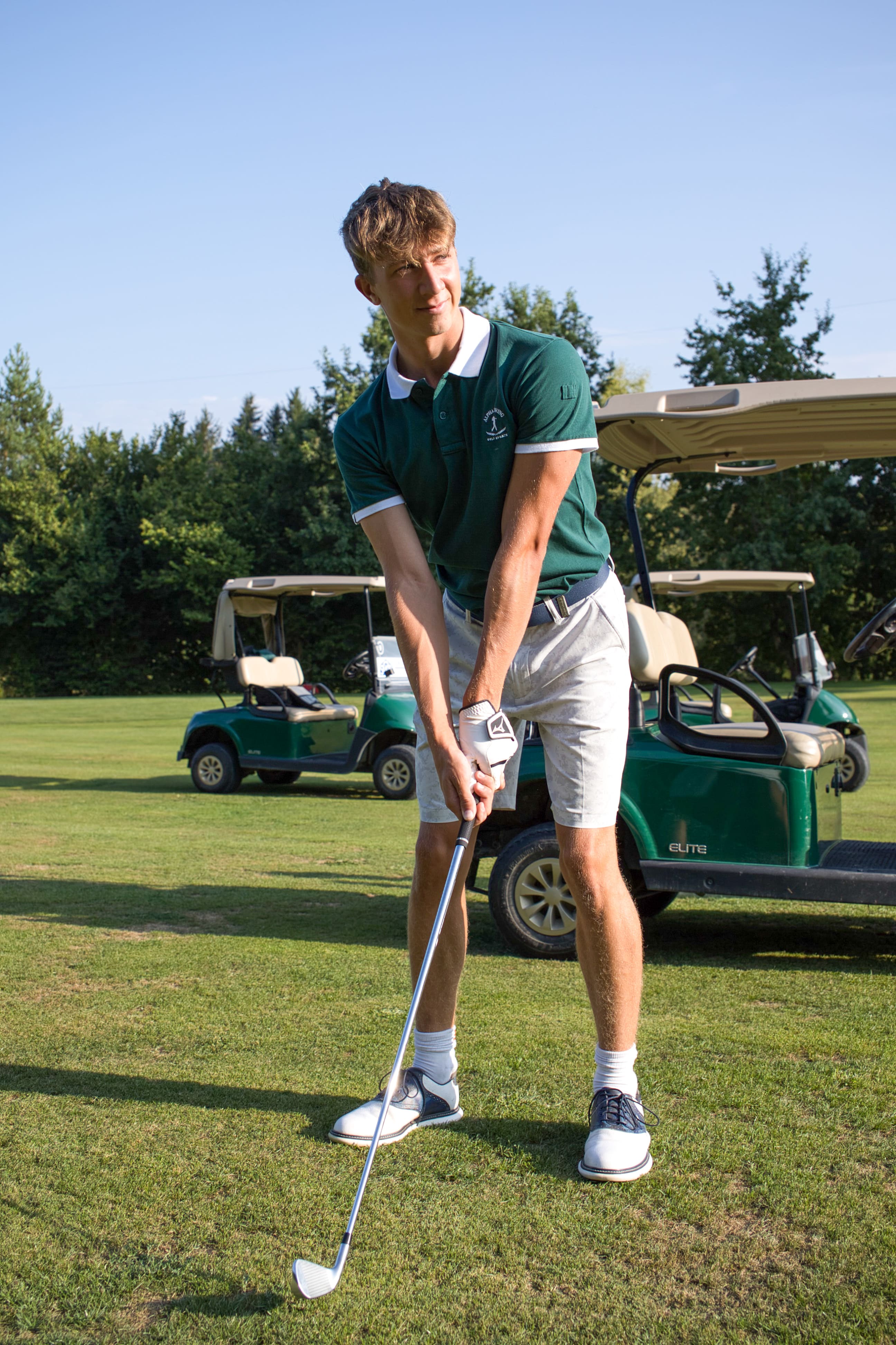 Männliches Model schlägt einen Golfball, während es das forest-grüne Alpha Swing Polo trägt. Ideal für stilvolle und funktionale Golfbekleidung