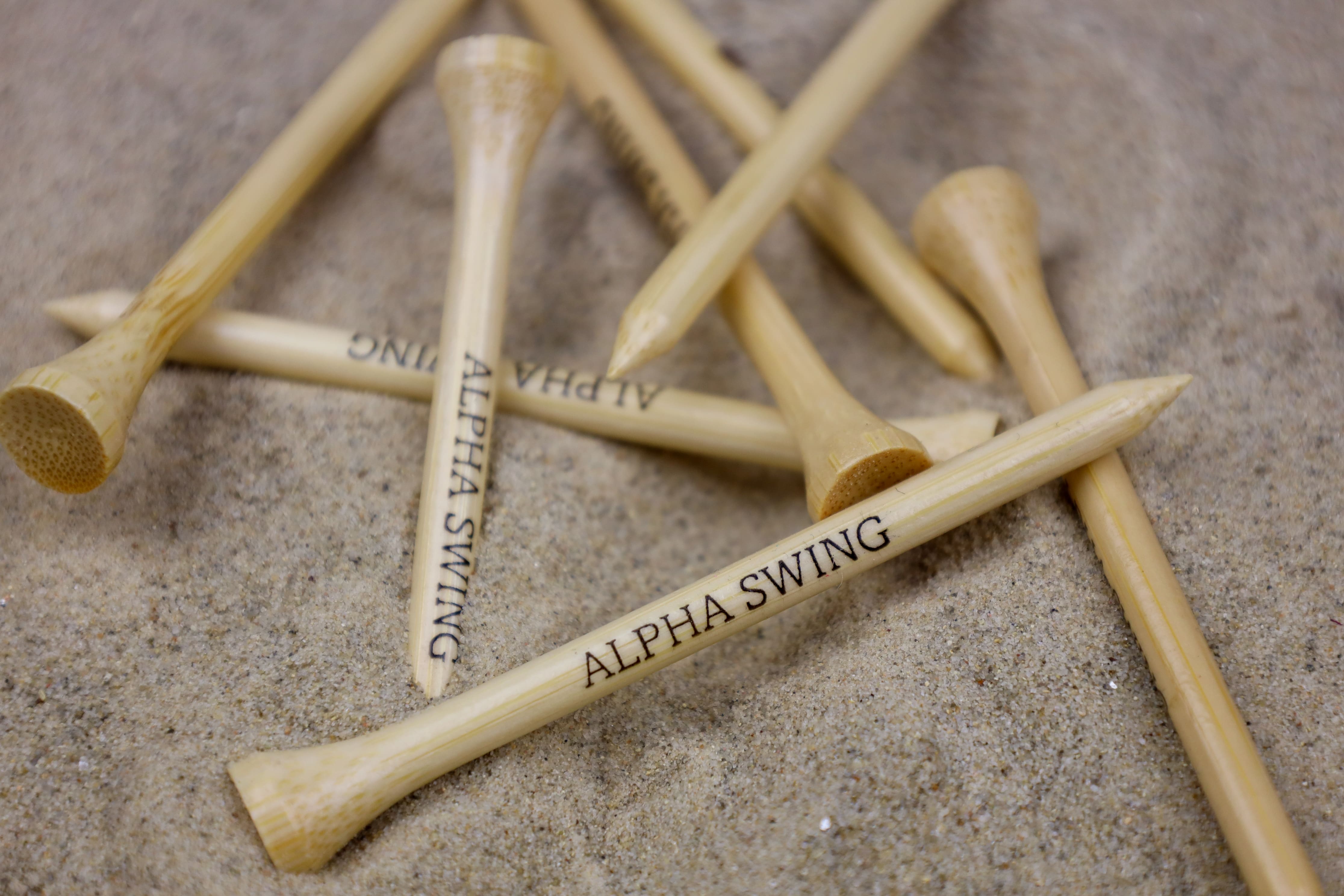 Alpha Swing Golf Tees im Sand. 100% natürliche Bambus-Tees, ideal für einen umweltbewussten Golfschwung.
